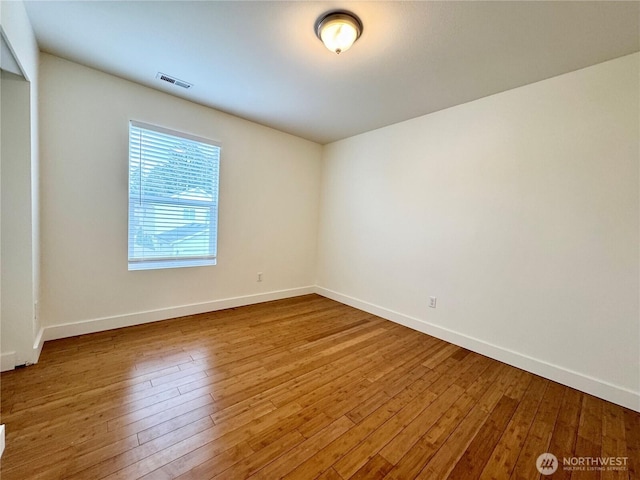 spare room with hardwood / wood-style floors, baseboards, and visible vents