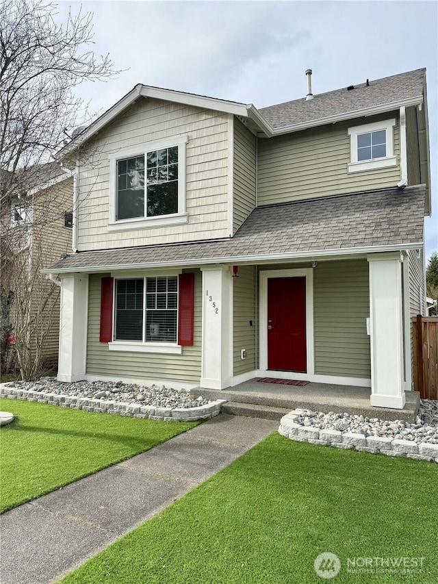 traditional home featuring roof with shingles, covered porch, and a front lawn