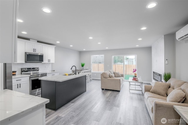 kitchen with a sink, white cabinetry, open floor plan, appliances with stainless steel finishes, and backsplash