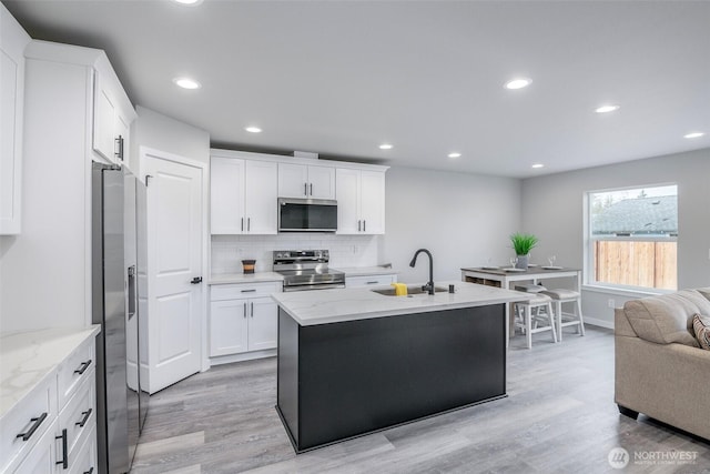 kitchen featuring appliances with stainless steel finishes, light wood-type flooring, a sink, and tasteful backsplash