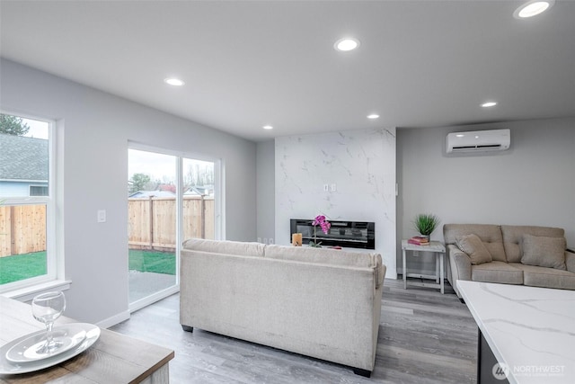 living room featuring recessed lighting, a premium fireplace, baseboards, light wood-type flooring, and a wall mounted air conditioner