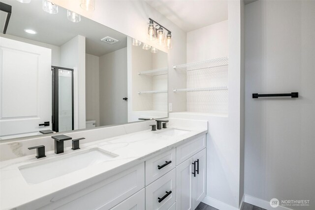 full bath with a sink, a shower stall, toilet, and double vanity