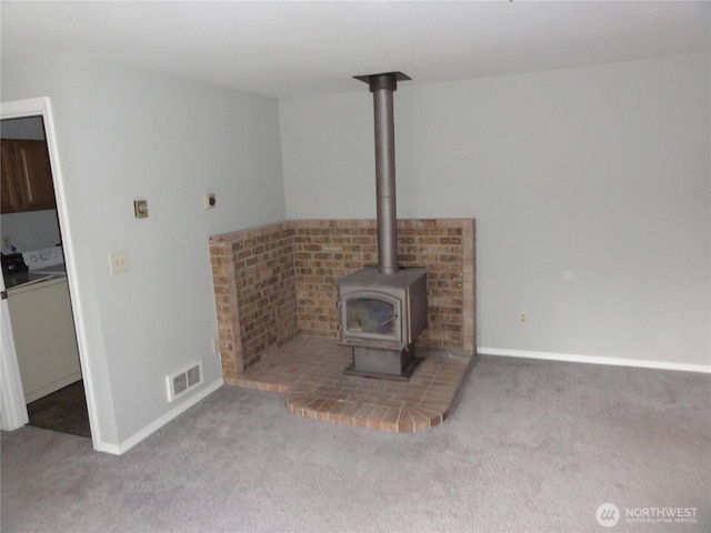 unfurnished living room with carpet floors, visible vents, a wood stove, washer / dryer, and baseboards