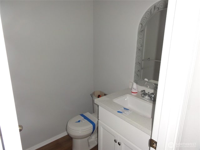 half bath with toilet, baseboards, and vanity