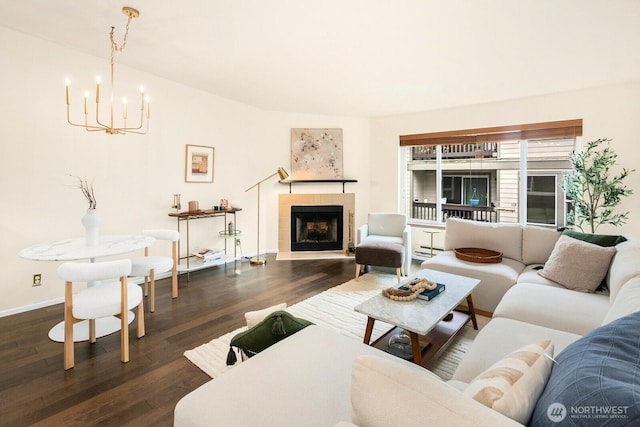 living room featuring a fireplace, dark wood finished floors, an inviting chandelier, and baseboards