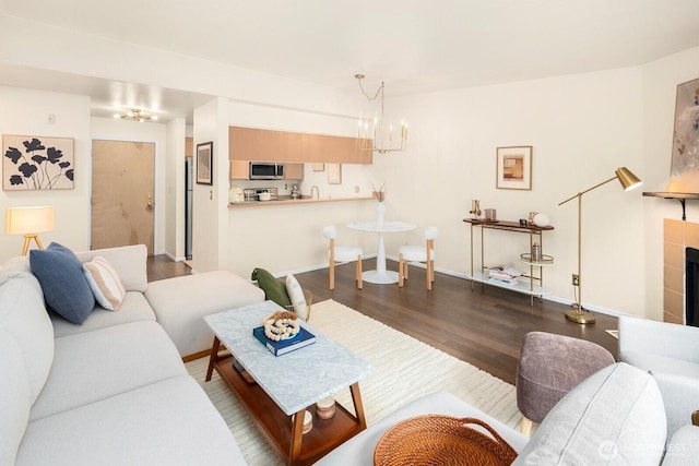 living area featuring dark wood-type flooring, baseboards, a tiled fireplace, and an inviting chandelier