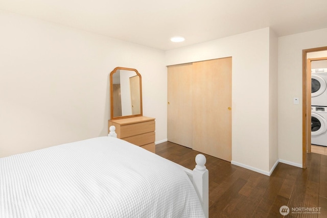 bedroom with a closet, stacked washer / dryer, wood finished floors, and baseboards