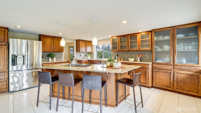 kitchen featuring a kitchen island, brown cabinets, black electric cooktop, a kitchen bar, and stainless steel refrigerator with ice dispenser