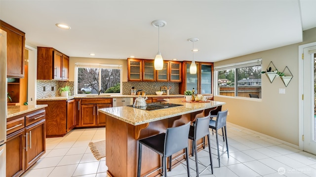 kitchen featuring brown cabinets, black electric stovetop, light tile patterned floors, glass insert cabinets, and a sink