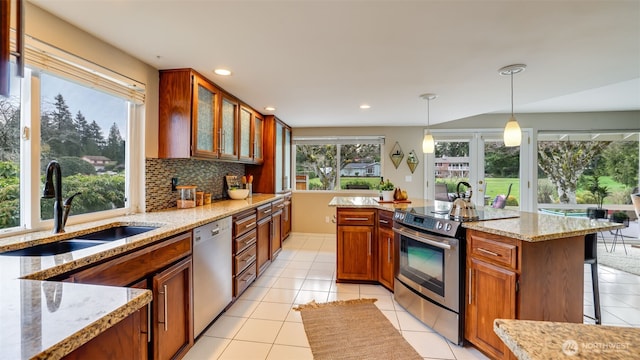 kitchen featuring brown cabinets, stainless steel appliances, decorative backsplash, a sink, and light stone countertops