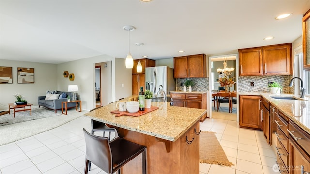 kitchen with light tile patterned flooring, a sink, open floor plan, stainless steel refrigerator with ice dispenser, and decorative backsplash