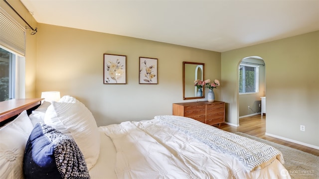 bedroom with arched walkways, wood finished floors, and baseboards