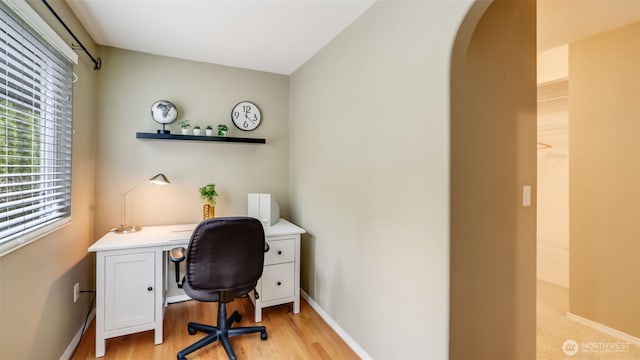 office area with light wood finished floors, baseboards, and arched walkways