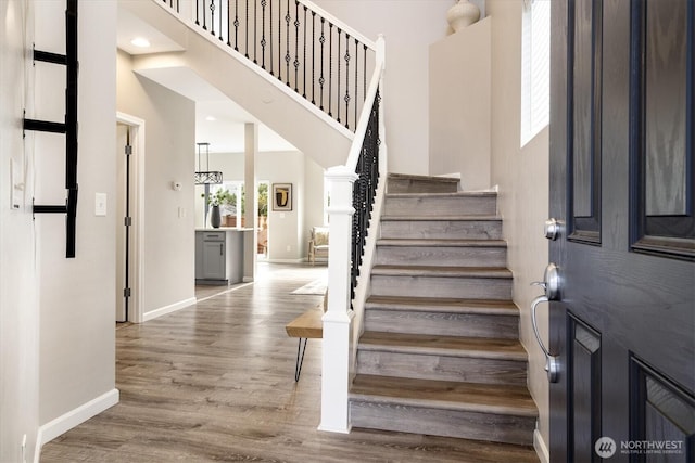 stairs featuring a towering ceiling, baseboards, and wood finished floors