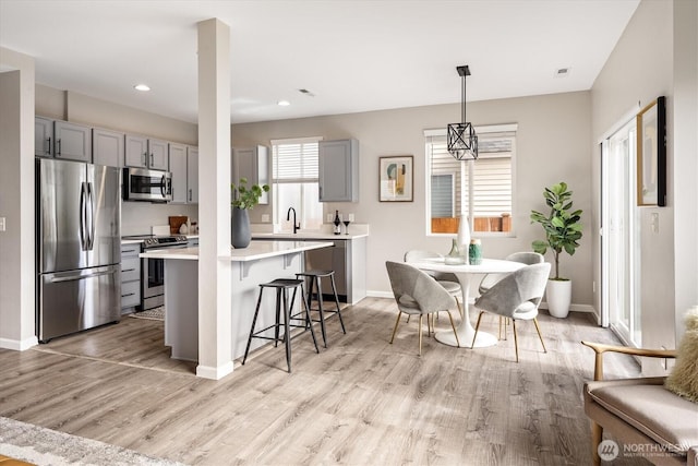 kitchen featuring gray cabinetry, a breakfast bar, light countertops, light wood-style floors, and stainless steel appliances