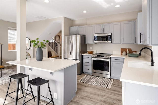 kitchen with light wood finished floors, a sink, gray cabinetry, stainless steel appliances, and a kitchen bar