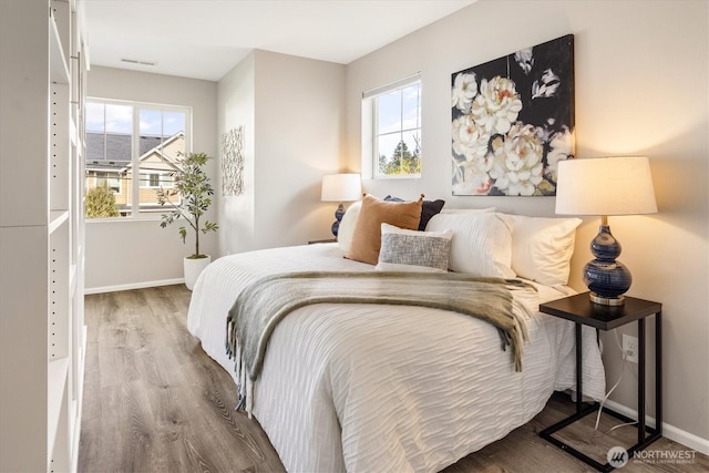 bedroom with multiple windows, wood finished floors, and baseboards