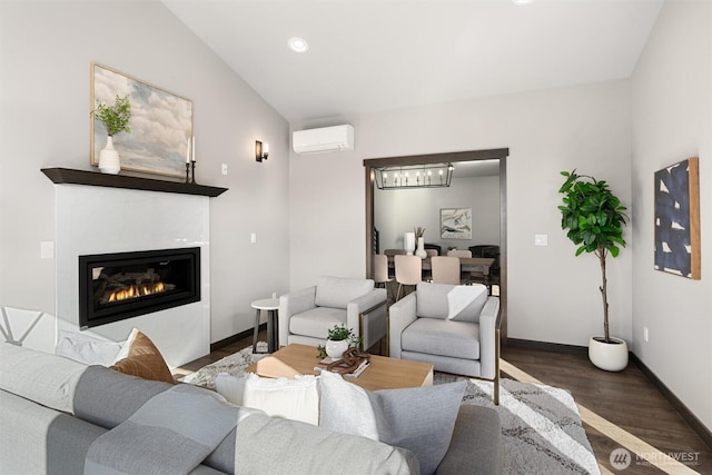 living area with lofted ceiling, wood finished floors, baseboards, a wall mounted AC, and a glass covered fireplace