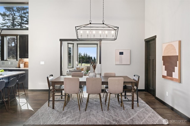 dining area featuring dark wood-type flooring, a chandelier, baseboards, and a high ceiling