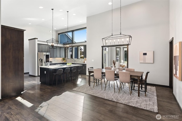 dining room featuring an inviting chandelier, baseboards, high vaulted ceiling, and dark wood-type flooring