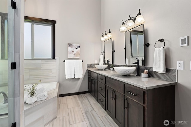 bathroom with a garden tub, double vanity, an enclosed shower, a sink, and baseboards