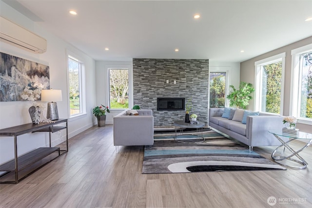 living area with a fireplace, wood finished floors, a wealth of natural light, and a wall mounted air conditioner