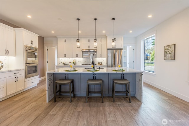 kitchen with decorative backsplash, light wood-style flooring, a breakfast bar area, stainless steel appliances, and white cabinetry