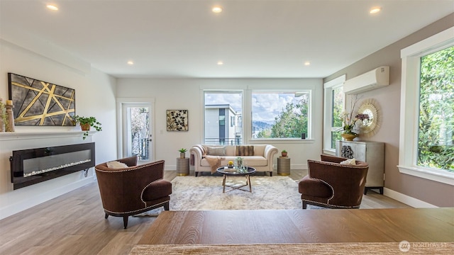 living area with recessed lighting, wood finished floors, baseboards, an AC wall unit, and a glass covered fireplace