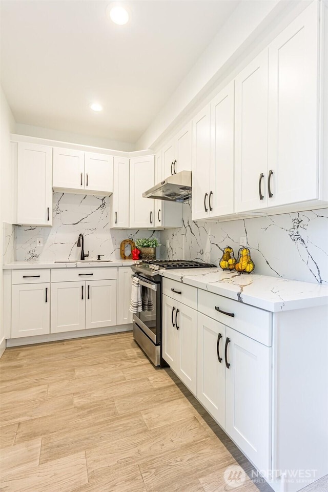 kitchen featuring white cabinets, light wood-style floors, stainless steel range with gas stovetop, under cabinet range hood, and a sink