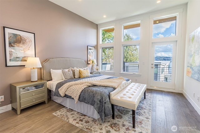 bedroom with recessed lighting, wood finished floors, a towering ceiling, baseboards, and access to exterior