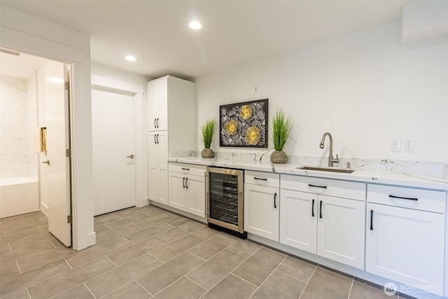 kitchen with light stone counters, recessed lighting, white cabinets, a sink, and beverage cooler