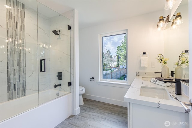 bathroom featuring shower / bath combination with glass door, double vanity, toilet, a sink, and baseboards