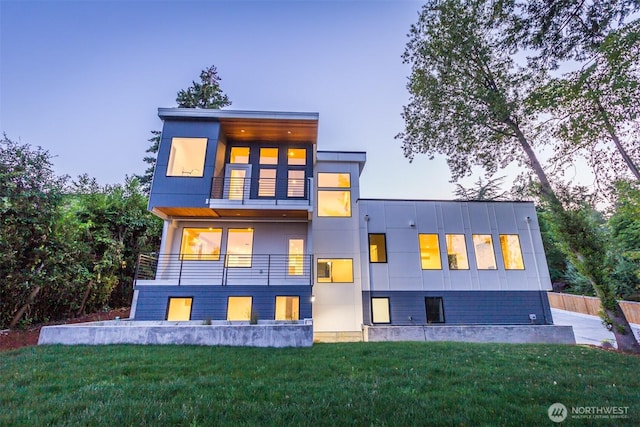 back of house featuring a lawn, a balcony, and stucco siding