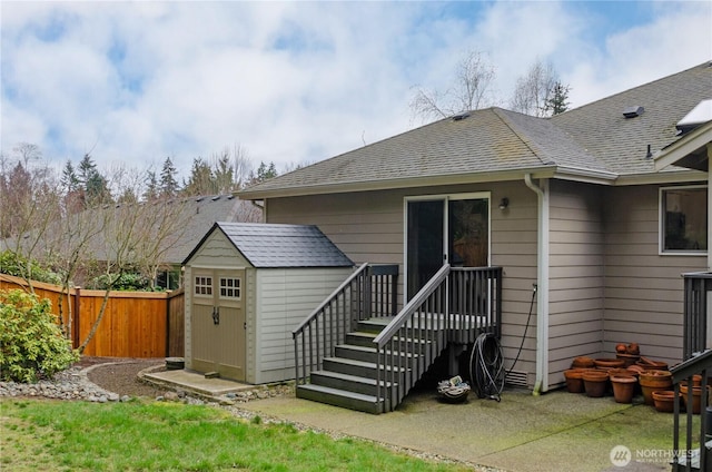 rear view of house with a storage shed, roof with shingles, an outdoor structure, and fence private yard