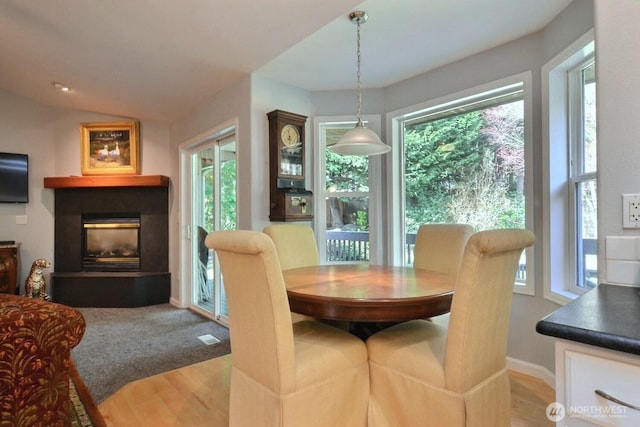 dining area with vaulted ceiling, wood finished floors, a glass covered fireplace, and baseboards