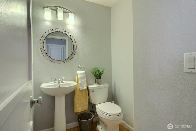 half bathroom with a sink, toilet, and baseboards