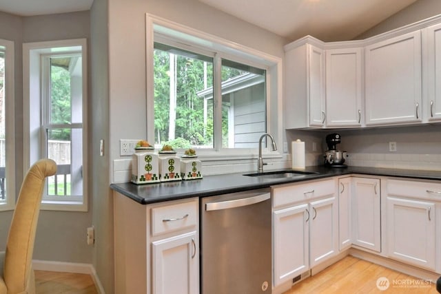 kitchen with a sink, white cabinets, light wood-style floors, stainless steel dishwasher, and dark countertops