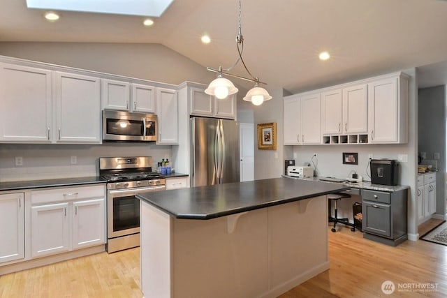 kitchen featuring stainless steel appliances, dark countertops, a center island, and light wood-style floors