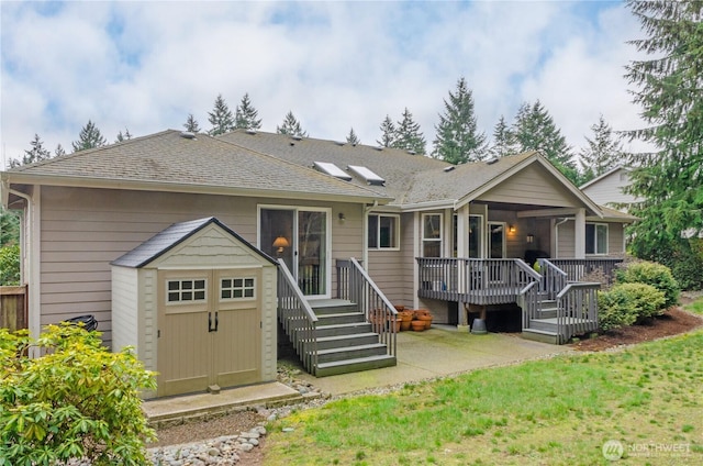 rear view of property with roof with shingles, a patio area, an outdoor structure, and a shed