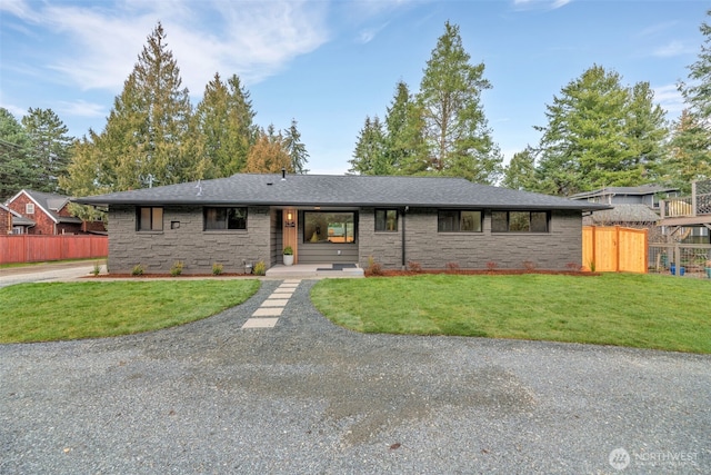 ranch-style house featuring a shingled roof, fence, and a front lawn