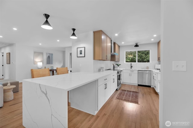 kitchen featuring a peninsula, light wood-type flooring, appliances with stainless steel finishes, and light stone counters