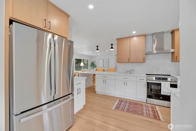 kitchen with recessed lighting, light countertops, appliances with stainless steel finishes, wall chimney range hood, and light wood-type flooring