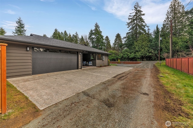 exterior space featuring a garage, concrete driveway, fence, and a shingled roof