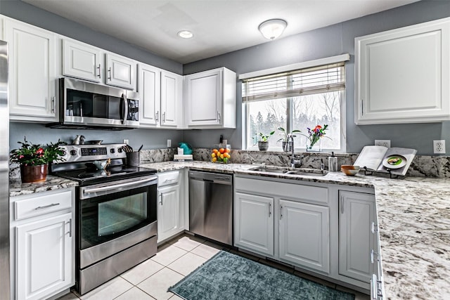 kitchen with stainless steel appliances, white cabinetry, a sink, and light tile patterned floors