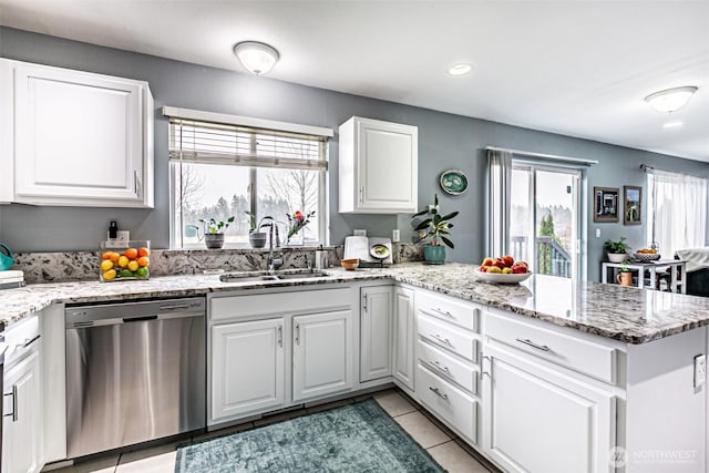 kitchen with light tile patterned floors, stainless steel dishwasher, white cabinetry, a sink, and a peninsula