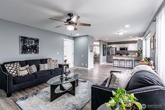 living area with light wood-type flooring, baseboards, a ceiling fan, and recessed lighting