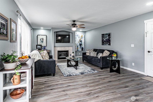 living room with ceiling fan, baseboards, wood finished floors, and a tile fireplace