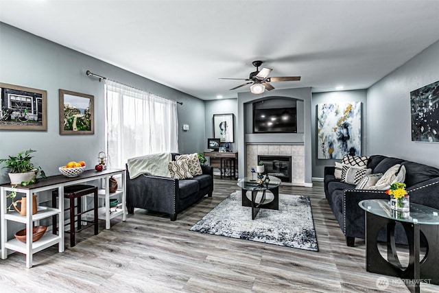 living area with a tiled fireplace, wood finished floors, a ceiling fan, and baseboards