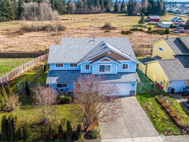 view of front of house featuring a garage, concrete driveway, roof with shingles, fence, and a front yard