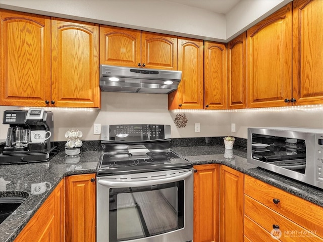 kitchen featuring under cabinet range hood, stainless steel appliances, dark stone countertops, and brown cabinetry